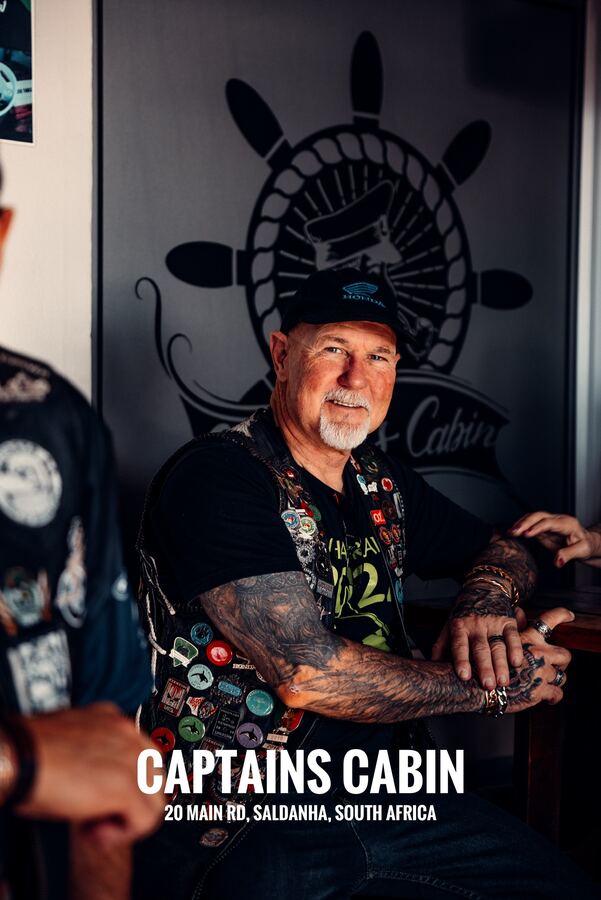 A rider in a badge-covered vest in front of the Captain's Cabin ship's wheel mural