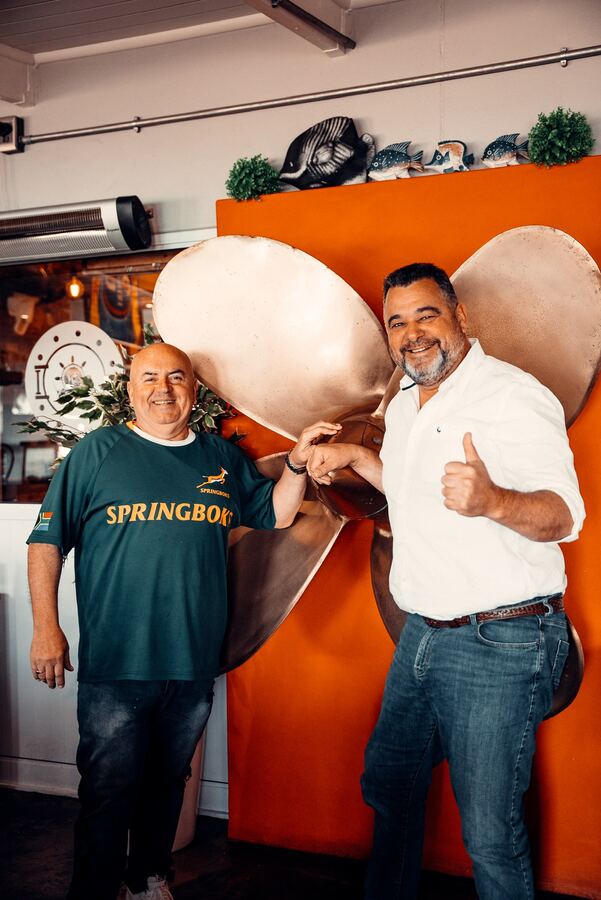 Two of the Captain's Cabin team beside the brass ship's propeller